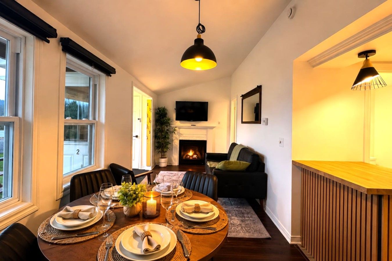 A dining area with a round table set for four, a fireplace, and a television mounted on the wall.