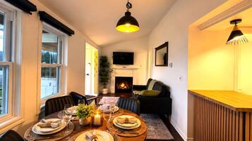 A dining area with a round table set for four, a fireplace, and a television mounted on the wall.