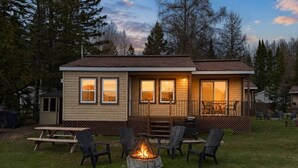 Eine kleine Holzhütte mit Terrasse, Sitzgelegenheit im Freien und einem Feuerkorb.