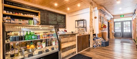 Interior de una cafetería con techo de madera, un menú en una pizarra y una barra con diversas bebidas y aperitivos.