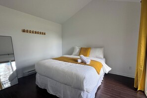 Quarto de hotel com cama, um cabideiro de madeira, janela e cortina.