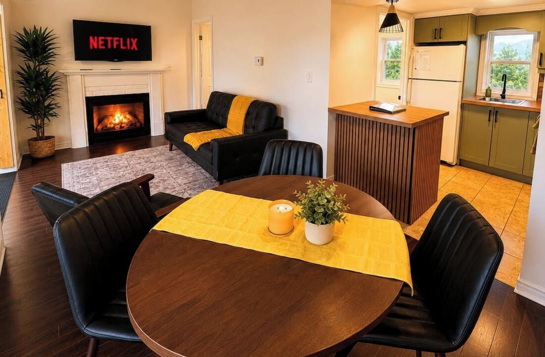 Un salon confortable avec une cheminée, un coin repas avec une table et des chaises, et une cuisine avec une fenêtre.