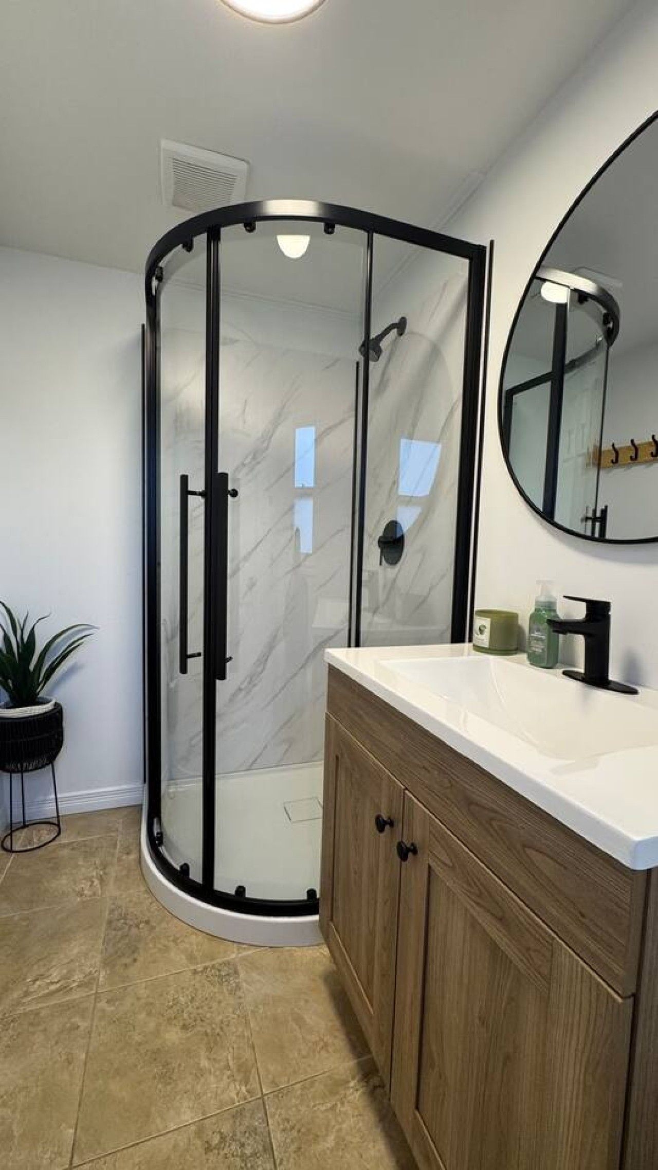 Une salle de bain moderne avec une douche à parois de verre, un meuble-lavabo en bois et un miroir rond.