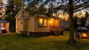 A wooden cabin with a porch, a hot tub, and a fire pit. - Le Fainéant | Spa, plage & art de ne rien faire (Sainte-Lucie-des-Laurentides)