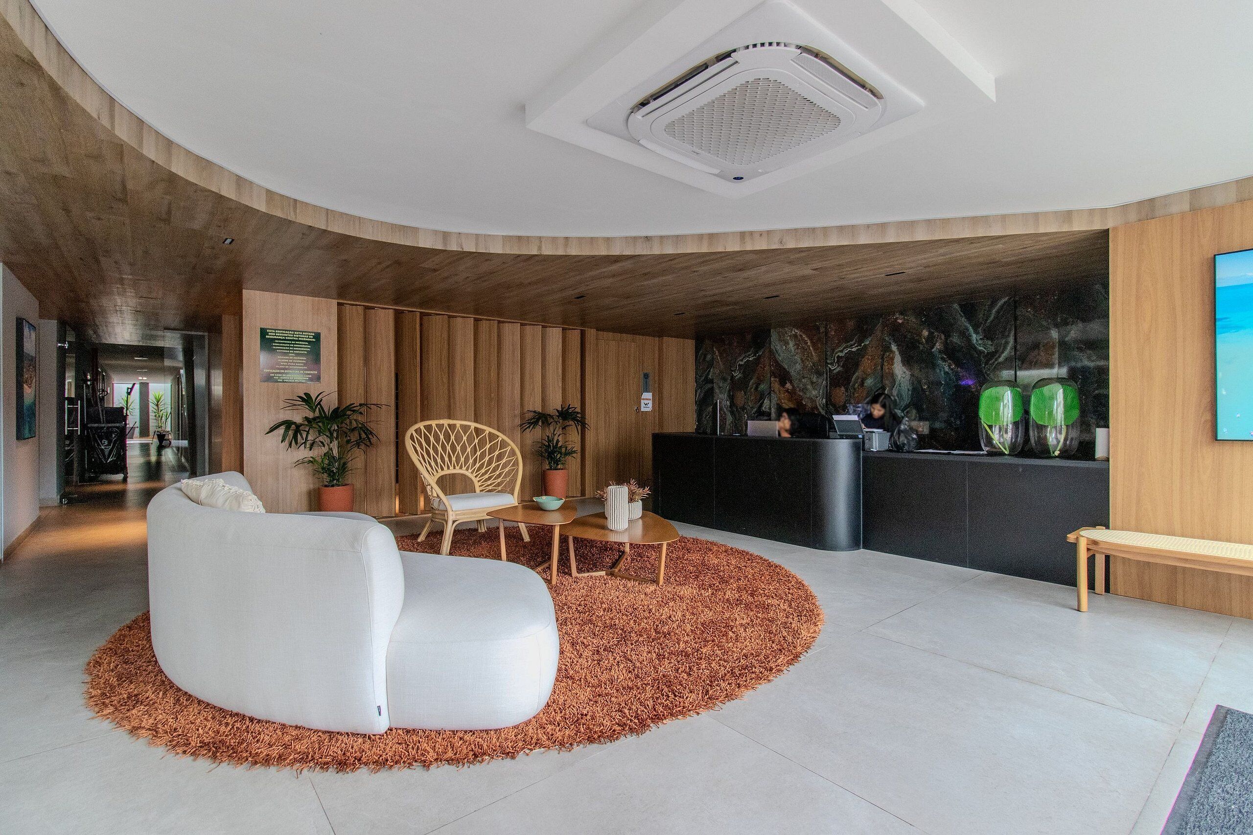 Uma área de recepção moderna com teto curvo, balcão de atendimento, sofá branco, banco de madeira e tapete estampado.