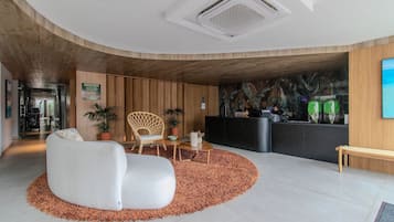 Uma área de recepção moderna com teto curvo, balcão de atendimento, sofá branco, banco de madeira e tapete estampado.