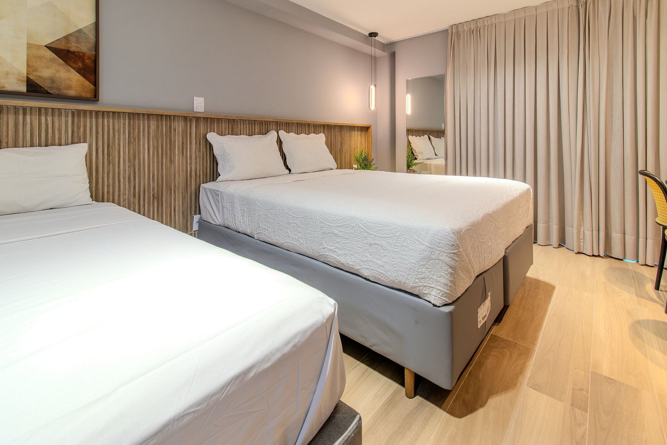 Een hotelkamer met twee bedden, een houten hoofdbord, een grote spiegel en een gordijn.