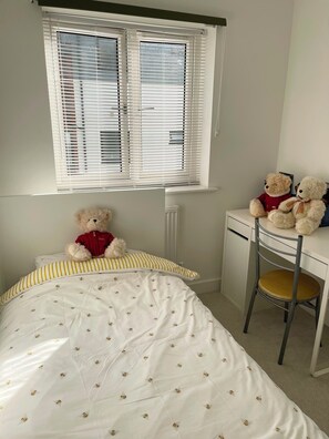 A bedroom with a bed, a desk, and a window with blinds.