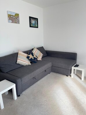 A modern living room with a grey sectional sofa, a white coffee table, and a small white side table with a remote control.