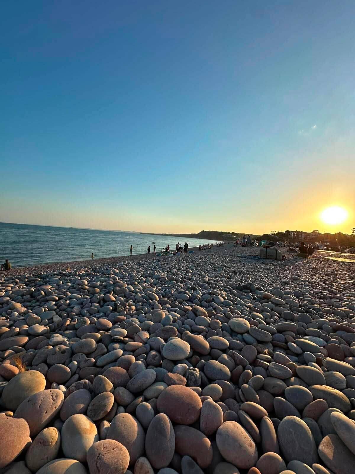 Una playa de guijarros con cielo despejado y el sol poniéndose al fondo.