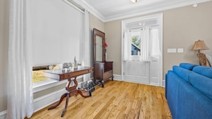 A room with a wooden floor, a blue sofa, a wooden desk with drawers, a mirror, and a white door. - Elegant Home in Prime Location/ Close to Universities, Hospitals, Parks and Stadiums (Atlanta)