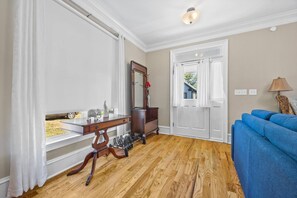 A room with a wooden floor, a blue sofa, a wooden desk with drawers, a mirror, and a white door. - Elegant Home in Prime Location/ Close to Universities, Hospitals, Parks and Stadiums (Atlanta)