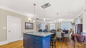 A kitchen with a blue island, wooden flooring, pendant lighting, and a dining area with a table and chairs. - Elegant Home in Prime Location/ Close to Universities, Hospitals, Parks and Stadiums (Atlanta)