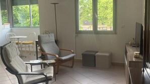 Un soggiorno con divano, poltrone, tavolino, televisore e una finestra vista alberi.