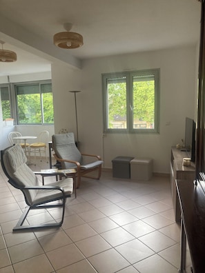Un salon comprenant un canapé, des fauteuils, une table basse, un téléviseur et une fenêtre donnant sur des arbres.