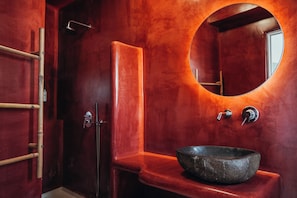 Ein Badezimmer mit rundem Spiegel, einem Waschbecken und einer Duschkabine.