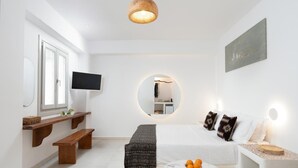 En moderne stue med fjernsyn, et rundt spejl, en sofa med mønstrede puder, en bænk og et lille bord med frugt.