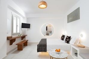 Ein modernes Wohnzimmer mit Fernseher, einem runden Spiegel, einer Couch mit gemusterten Kissen, einer Bank und einem kleinen Tisch mit Obst.