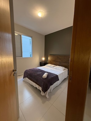 Une chambre à coucher avec un lit, une table de chevet, une fenêtre avec des stores et un luminaire au plafond.
