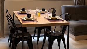 Zona de dinar amb una taula preparada per a quatre persones, quatre caires, una làmpada penjant i un sofà al fons.