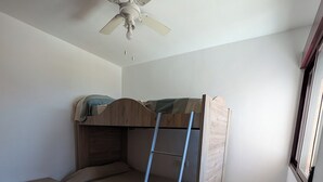 Quarto com beliche, ventoinha no teto, escada e cômoda pequena.