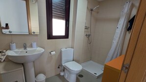 Uma casa de banho com lavatório, sanita, chuveiro e espelho.