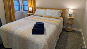 Un llit ben fet amb una manta doblegada, dues làmpades de nit i una finestra amb cortines.