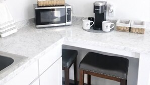 A compact kitchen with a microwave, coffee maker, and two stools.
