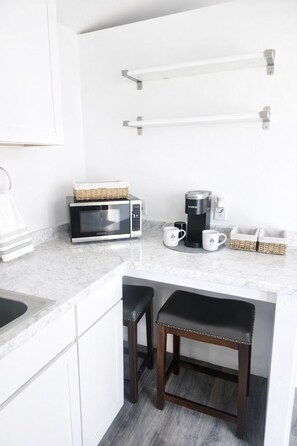 A compact kitchen with a microwave, coffee maker, and two stools.