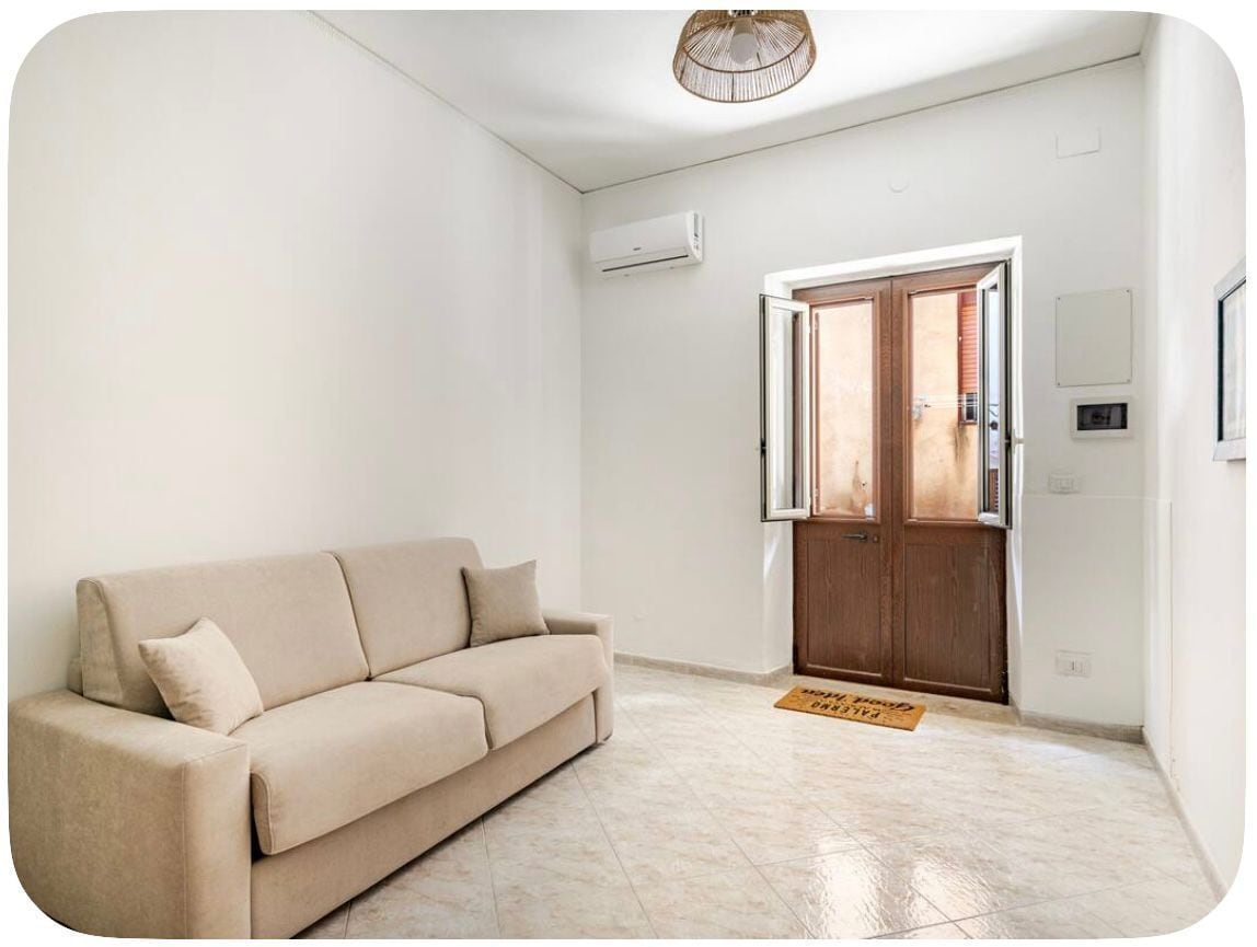 Un soggiorno con un divano color beige, una porta in legno e una parete bianca.