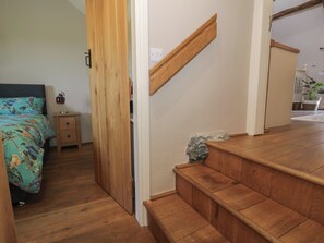 A bedroom with a bed, nightstand, and wooden staircase. - Beudy Bach (Llanbedr)