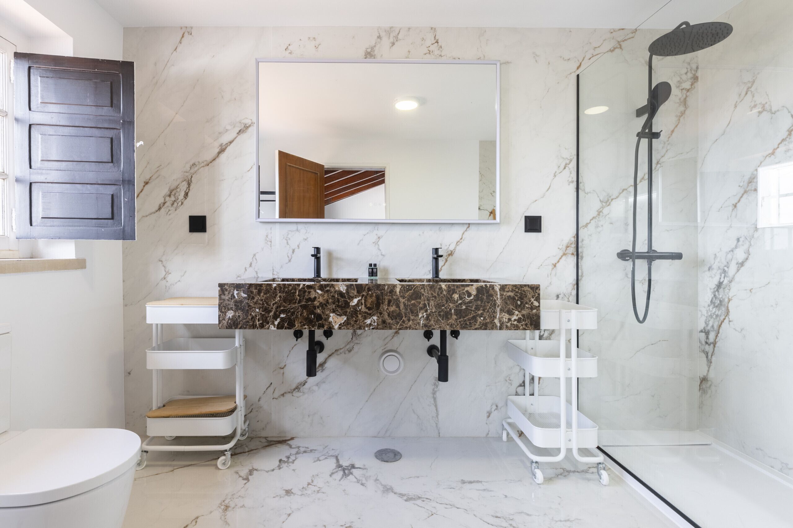 Une salle de bain avec un sol en marbre, un grand miroir, deux lavabos, une douche et des toilettes.