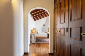 A hallway leading to a bedroom with a bed, a nightstand, and a lamp.