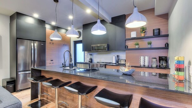 A modern kitchen with a central island, bar stools, stainless steel appliances, pendant lighting, and a microwave. - Stylish 5BR in Plateau Sleeps 10 (Montreal)