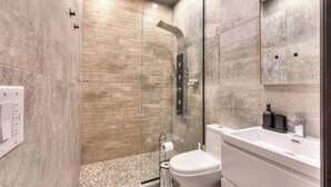 A modern bathroom with a glass-enclosed shower, a white toilet, and a sink with a mirror above. - Stylish 5BR in Plateau Sleeps 10 (Montreal)