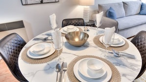 A round dining table with white plates, silverware, and a central gold bowl, surrounded by black leather chairs. - Stylish Plateau 1BR near Parc La Fontaine (Montreal)