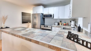 A modern kitchen with a stone countertop, stainless steel appliances, and white cabinetry.