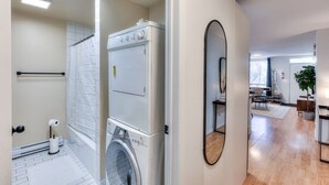 A laundry area with a washing machine and dryer, a mirror, and a hallway leading to a living space with a dining area.