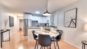 A modern kitchen with stainless steel appliances, a dining area with a round table and black chairs, and a bicycle-themed artwork on the wall.
