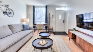 A modern living room with a sofa, coffee table, TV, and a bike mounted on the wall. - Stylish Plateau 1BR near Parc La Fontaine (Montreal)