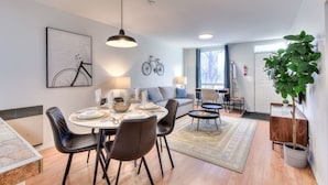 A modern living room with a dining area, a sofa, a coffee table, and a large potted plant. - Stylish Plateau 1BR near Parc La Fontaine (Montreal)