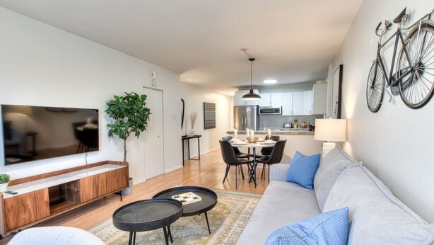 A modern living room with a sofa, coffee table, TV, and a dining area with chairs and a table.