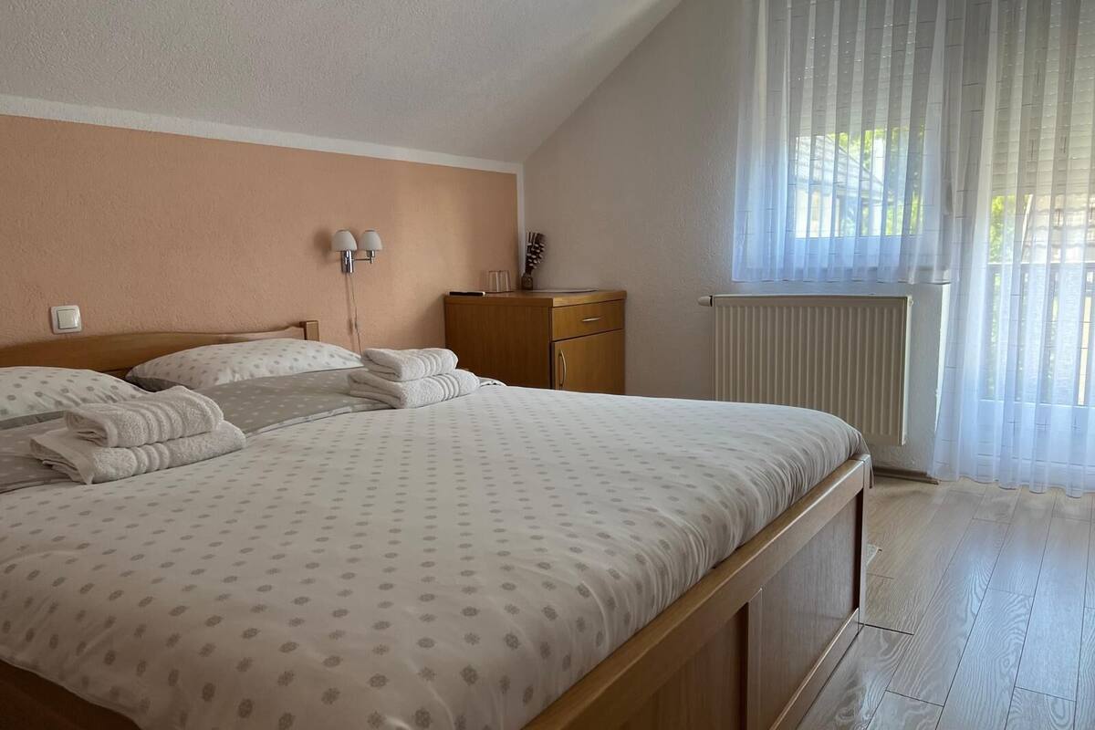 A bedroom with a bed, a nightstand, a dresser, a window with curtains, and a radiator.