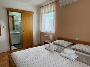 Une chambre d’hôtel avec une porte en bois donnant sur une salle de bain, un lit avec deux oreillers et une table de chevet avec une lampe.