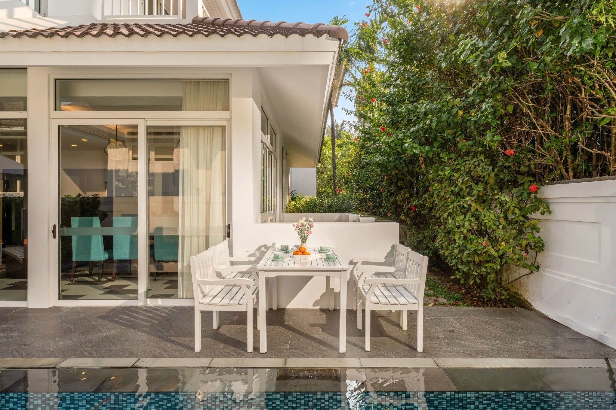 Un patio con una mesa, sillas, una puerta de vidrio que da a una habitación y una piscina.