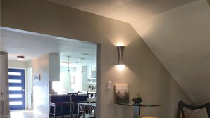 Un comedor con una mesa y sillas, una pequeña mesa redonda con dos sillas amarillas, y un aplique de pared.