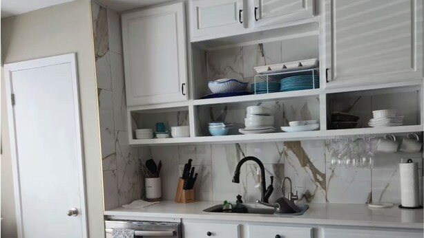 Una cocina con armarios blancos, salpicadero de mármol y encimera de madera.