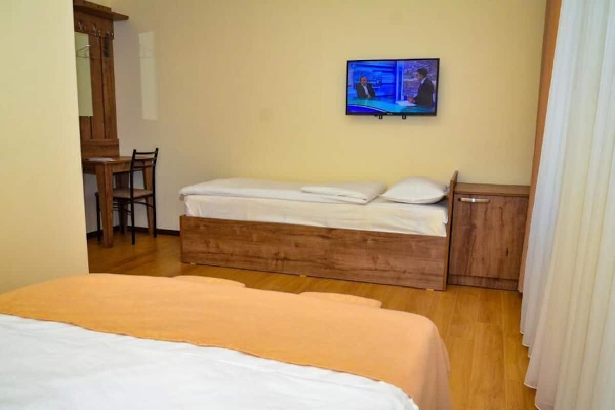 A room with a bed, a desk, a chair, a television, and a wooden cabinet.