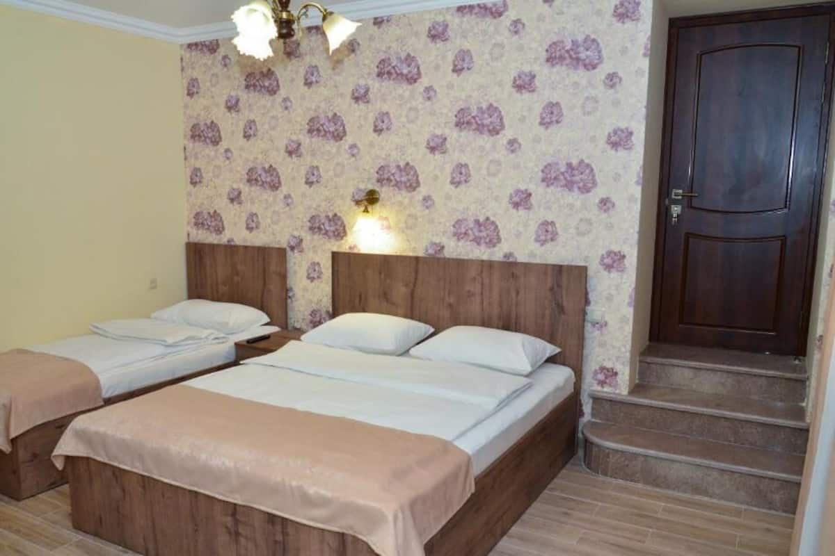 A room with two beds, a wooden headboard, a floral wallpaper, a door, and a staircase.
