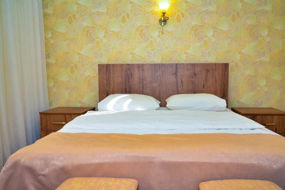 A hotel room with a wooden headboard, two bedside tables, a bed with white linens, and a floral wallpaper pattern.